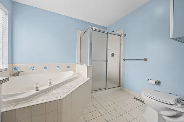 Primary bath corner tub beside the glass stall shower